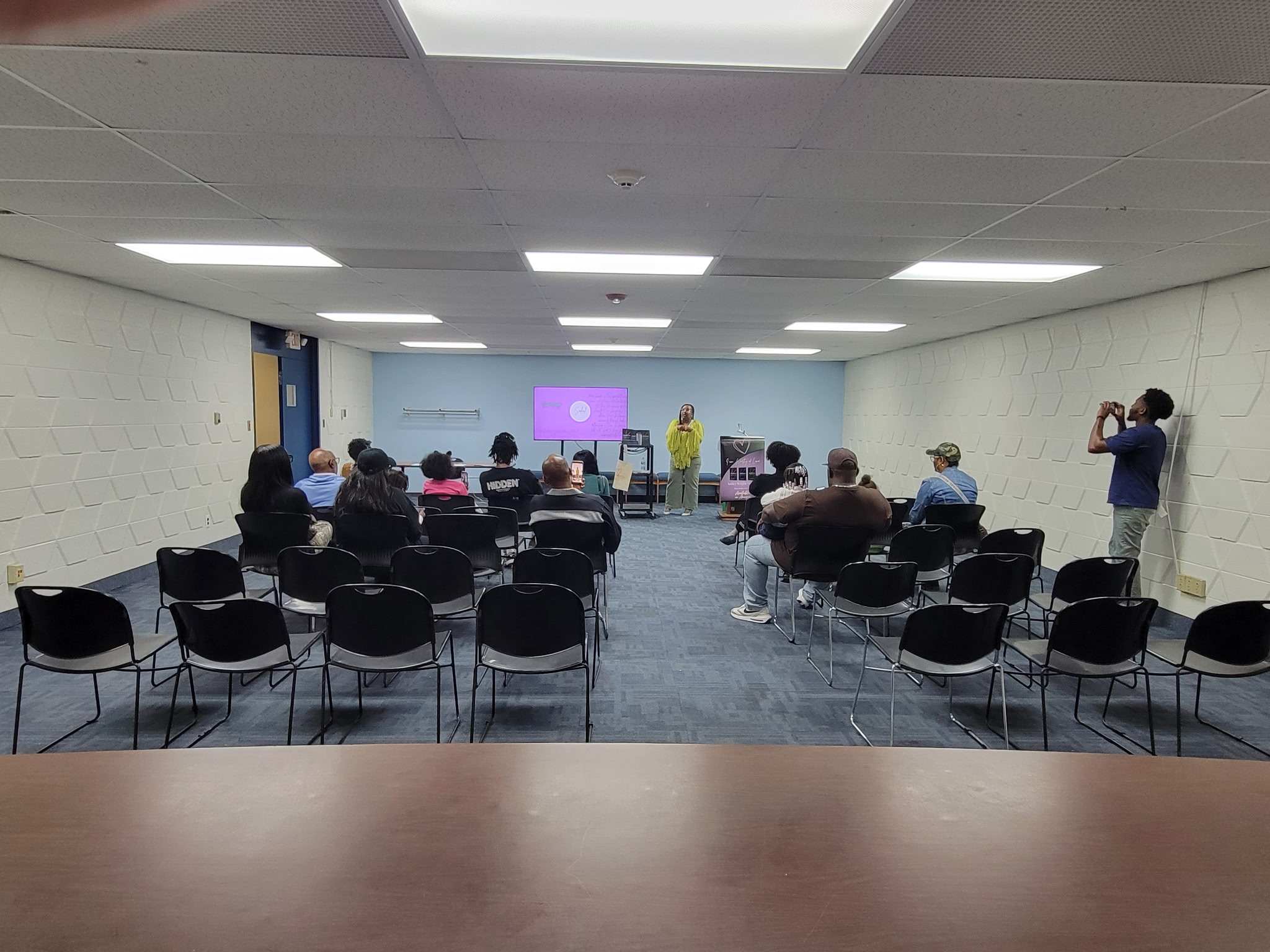 Author-Signing: Ashley Wright-McGhee on October 7th 2026: The picture shows the author talking about her books while showing a Power Point presentation with a laptop and TV. There are 12 participants.